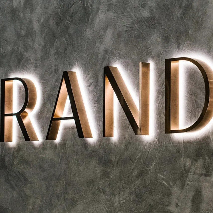 Reception sign with illuminated gold halo letters spelling brand name on textured wall