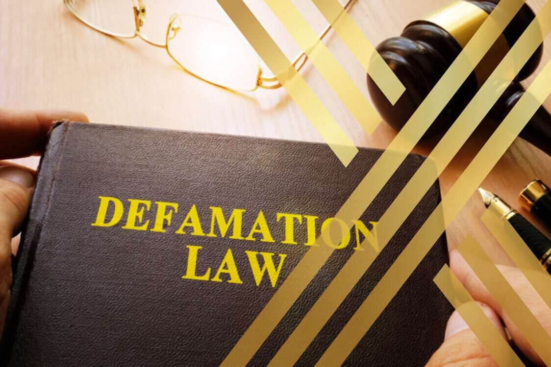 Close-up of a book titled "DEFAMATION LAW" next to a gavel and glasses.