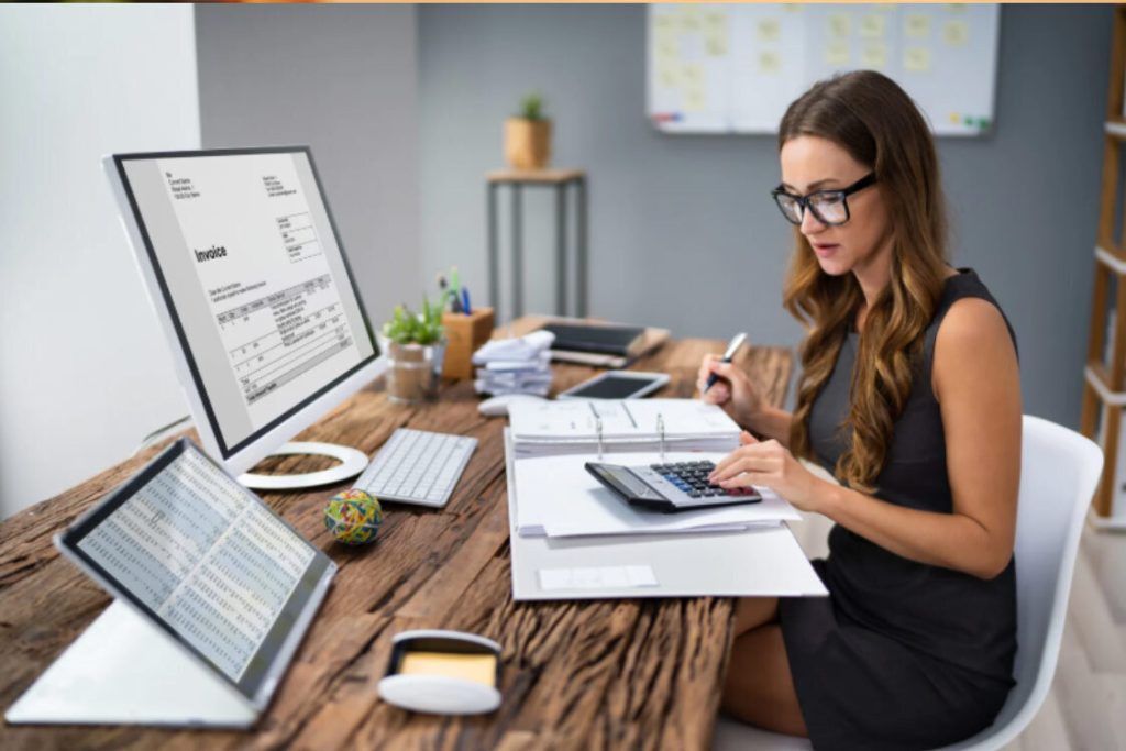 (Accountant using a calculator and computer to review a digital invoice, relating to identifying tax fraud.)