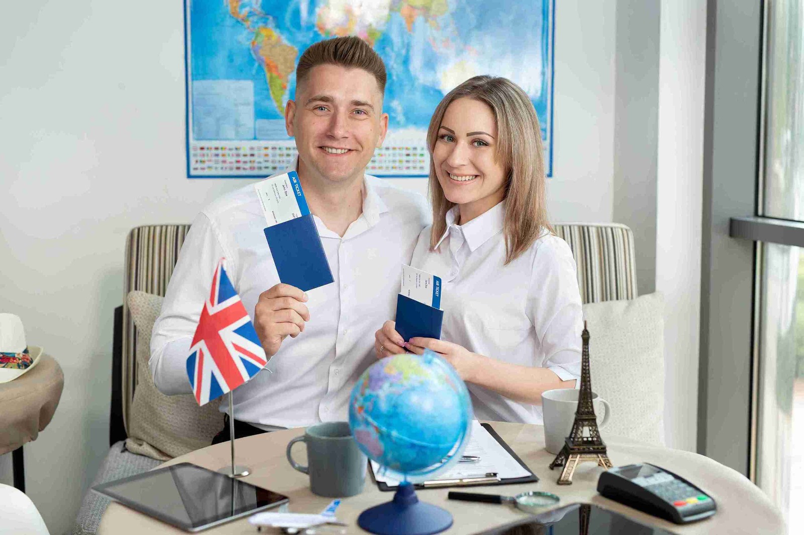 A man and woman smile while holding passports and a globe, symbolizing travel and adventure together.