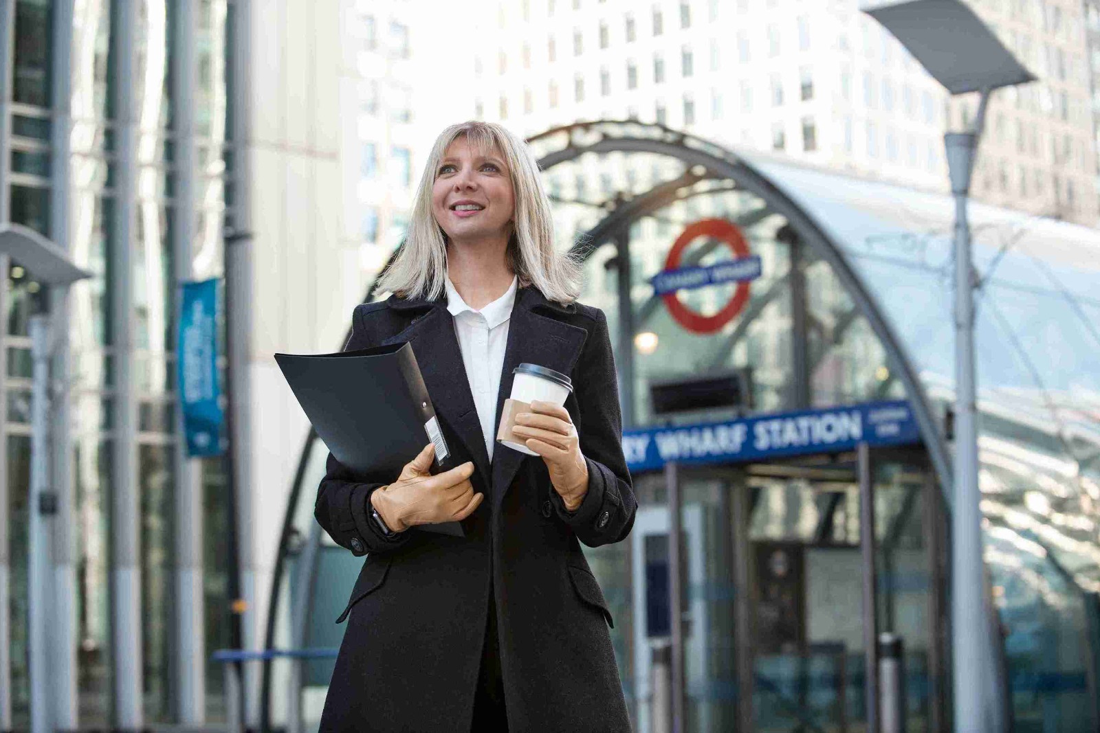 A woman in a business suit holds a coffee cup and a folder, looking confidently ahead in a professional setting.