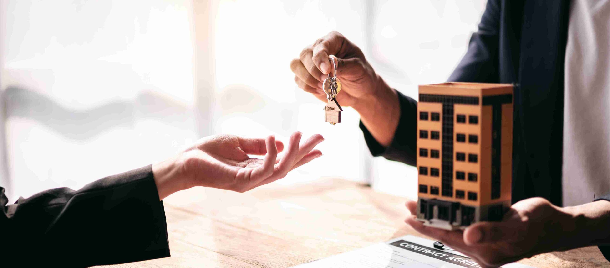 A man hands a key to a woman, who holds a model house, symbolizing a landlord-tenant agreement.