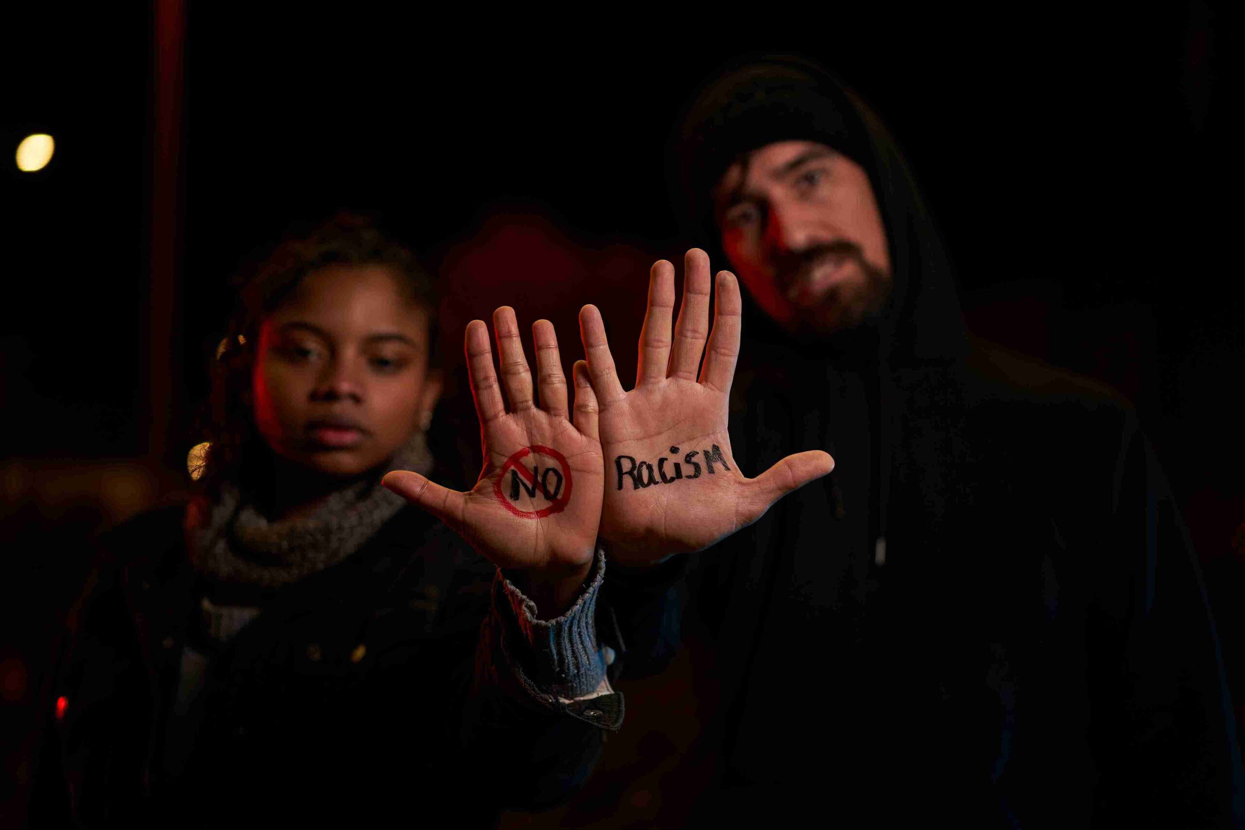 A man and woman raise their hands, displaying the word "no," symbolizing resistance against domestic abuse among migrants.