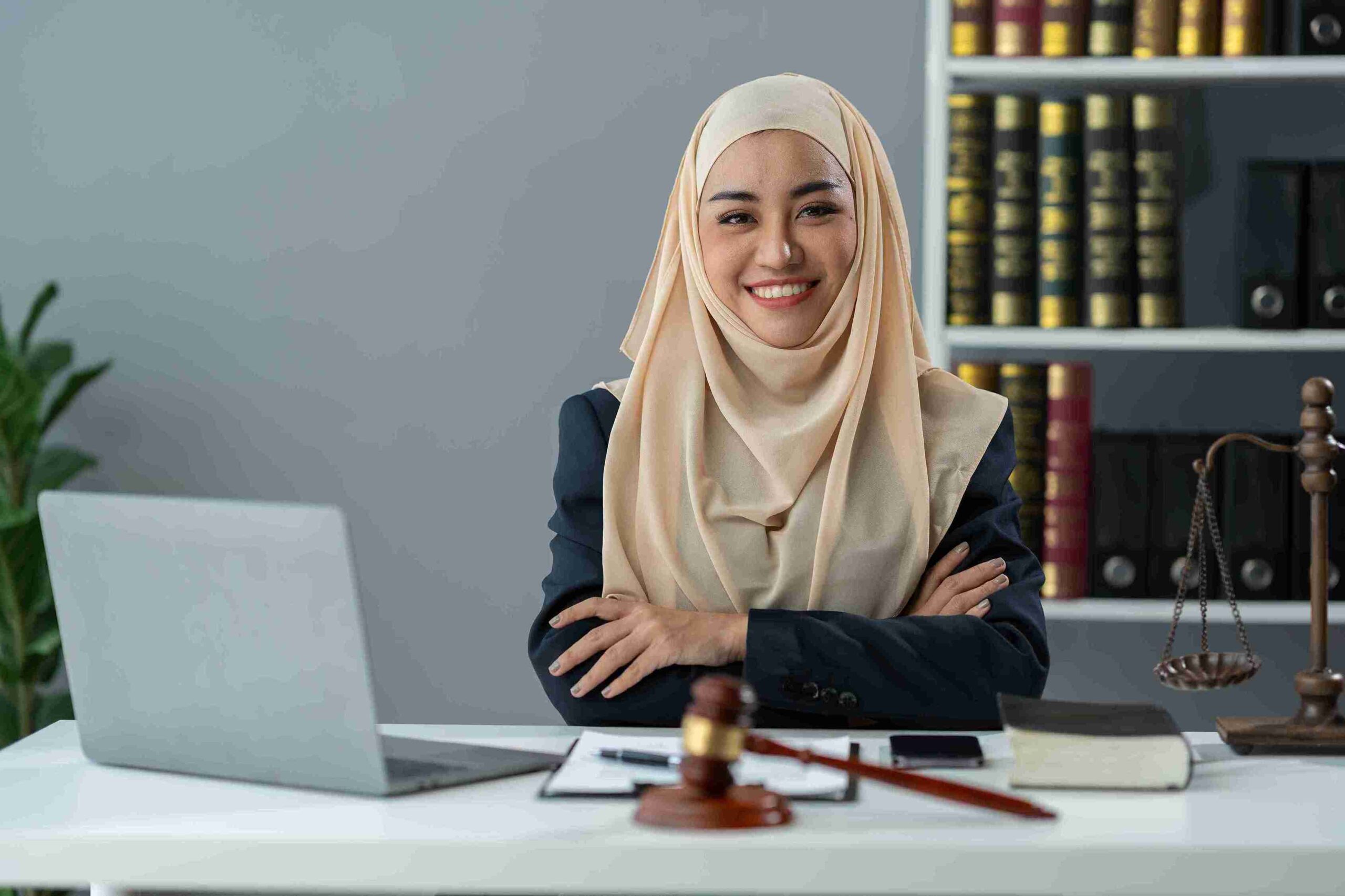 A woman in a hijab sits at a desk with a laptop, focused on her work related to human rights claims.