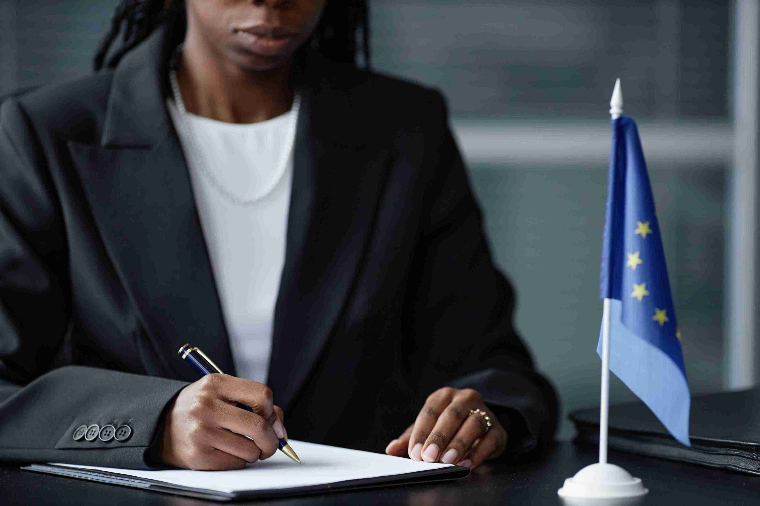 A woman in a business suit signs a contract, with an EU flag visible, symbolizing UK Sponsor agreements.