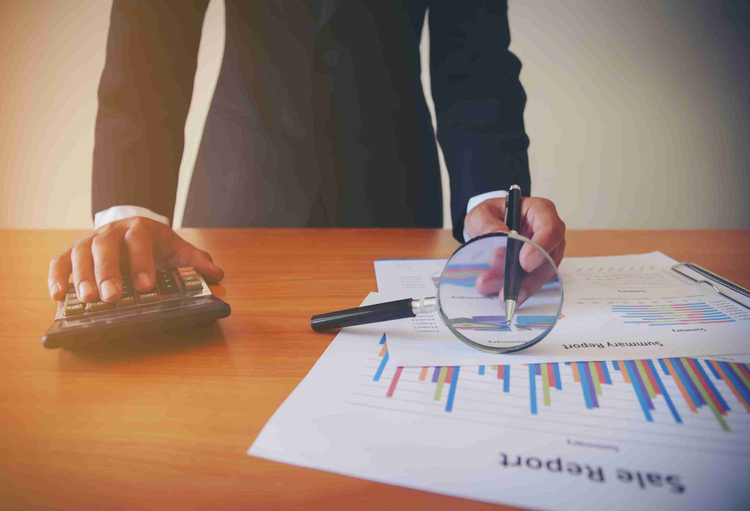 "Person in suit analysing sales report with magnifying glass and calculator, representing protecting businesses, and finances from tax investigations.