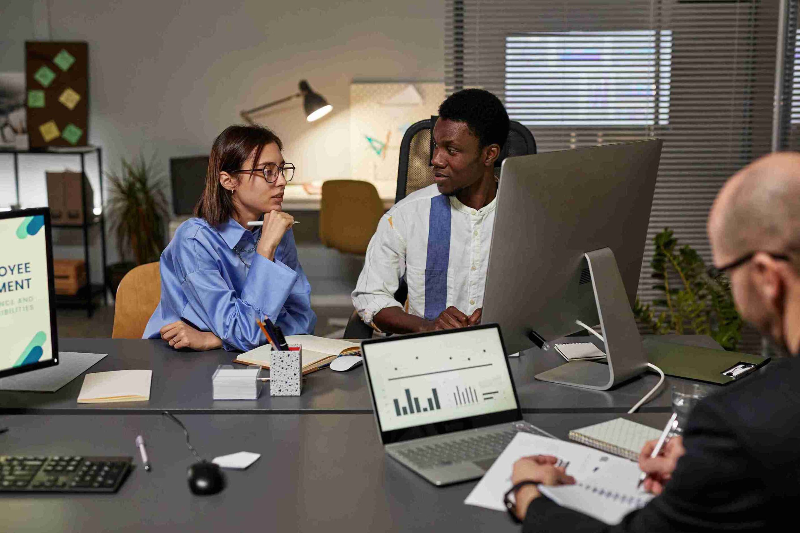 Three people collaborating at a table with a laptop and monitor, discussing Scale-Up VISA for attracting global talent