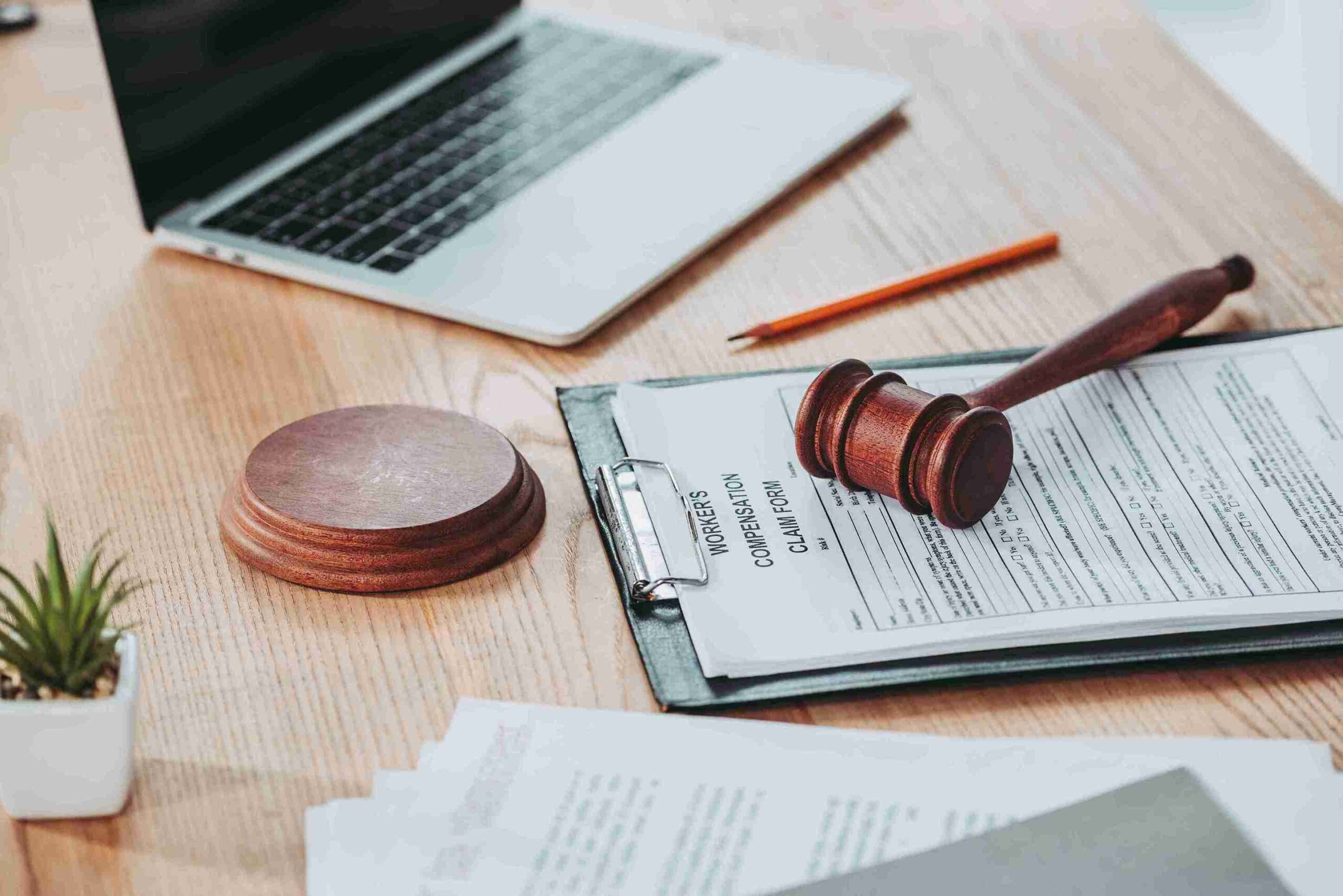A judge's gavel rests on a desk alongside a laptop and scattered papers, symbolizing legal proceedings and decision-making.