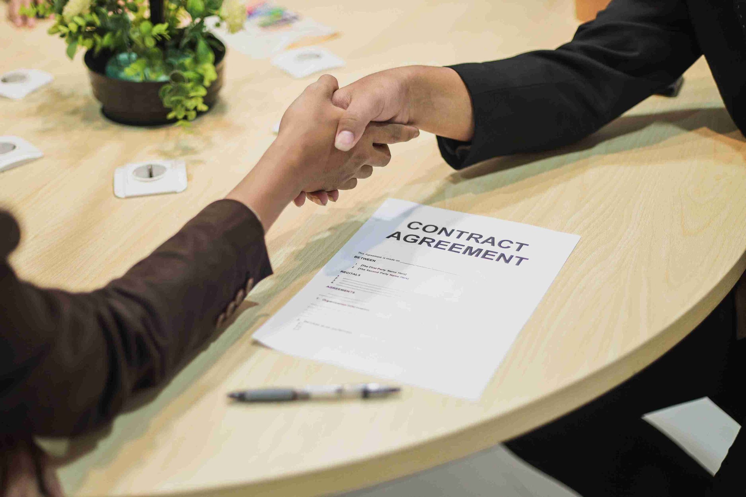 Two people shaking hands over a lease agreement, symbolizing a successful contract negotiation.