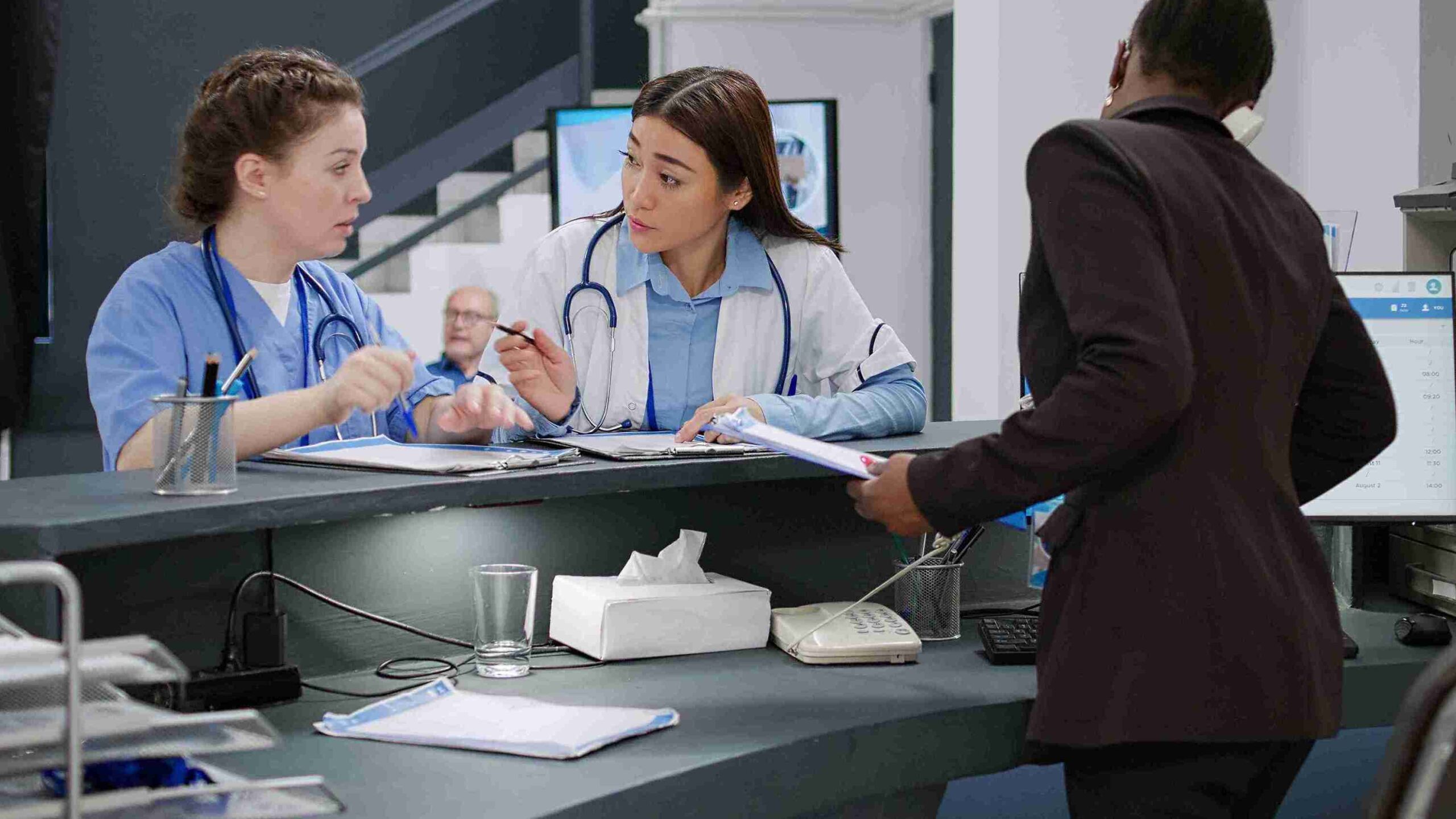 A woman wearing a blue coat stands confidently, smiling at the camera against a neutral background.