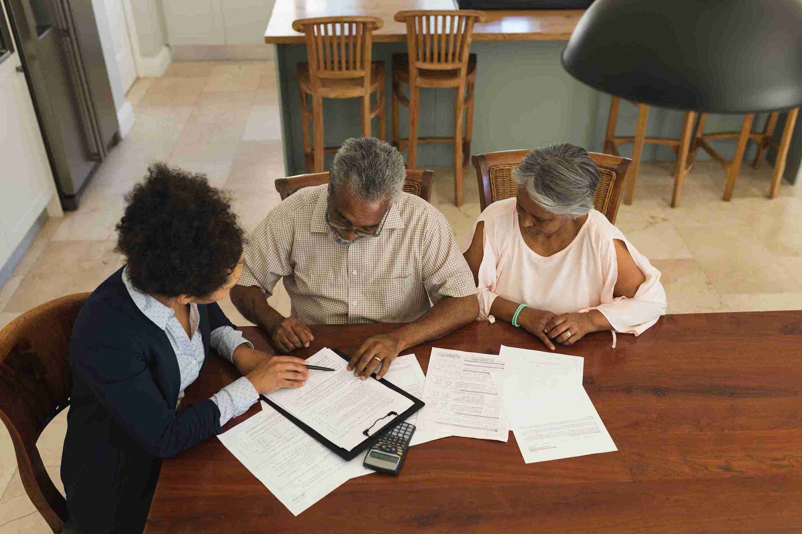 Woman assisting elderly couple with documents and calculator, representing estate planning to protect assets and manage taxes.