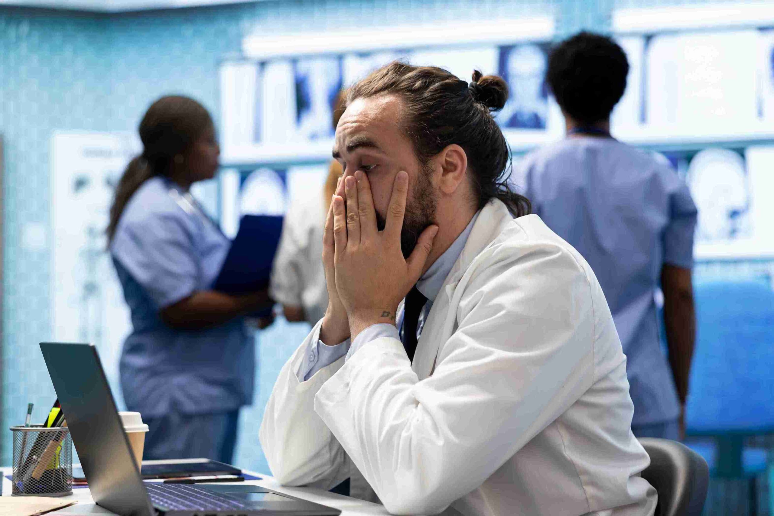 A man in a lab coat sits at a desk, hands on his face, reflecting on clinical negligence issues.