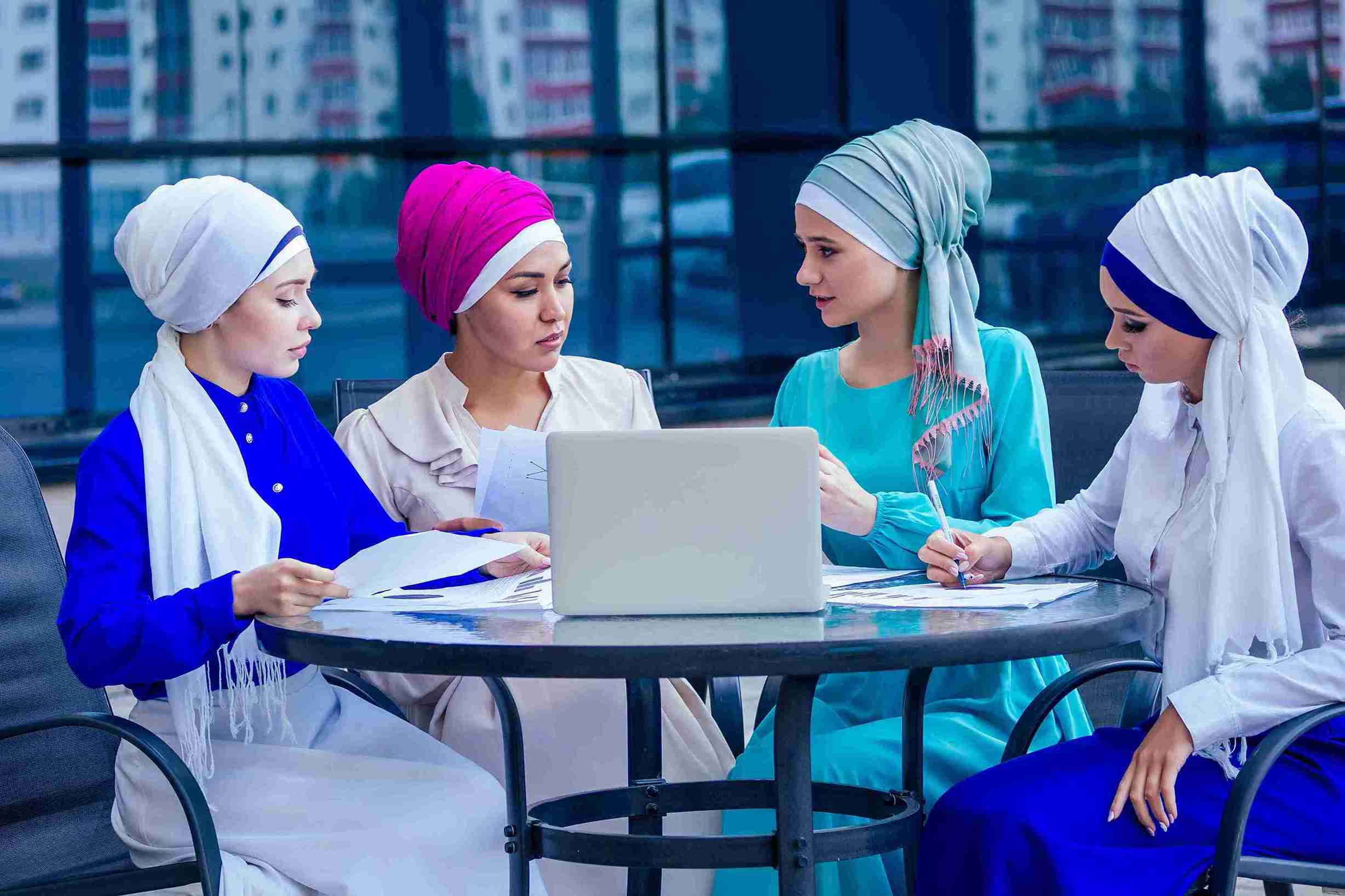 Four women in headscarves discussing documents and laptop outdoors, representing a Trust for financial planning and asset management."
