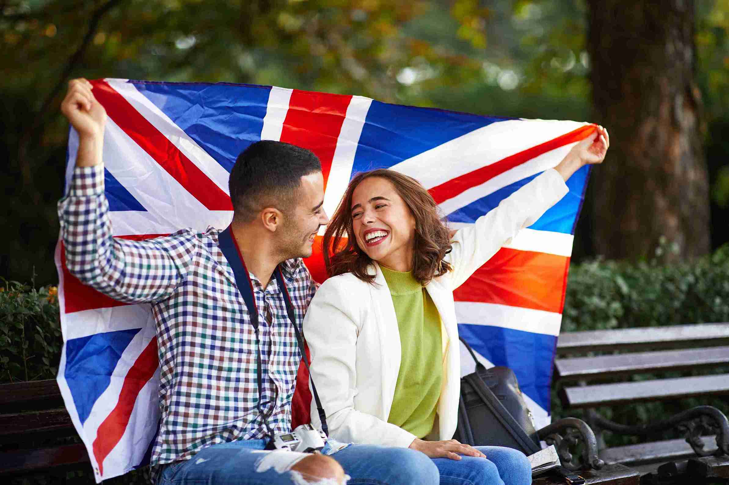 A couple sits on a bench, joyfully holding a British flag together, symbolizing unity and celebration.