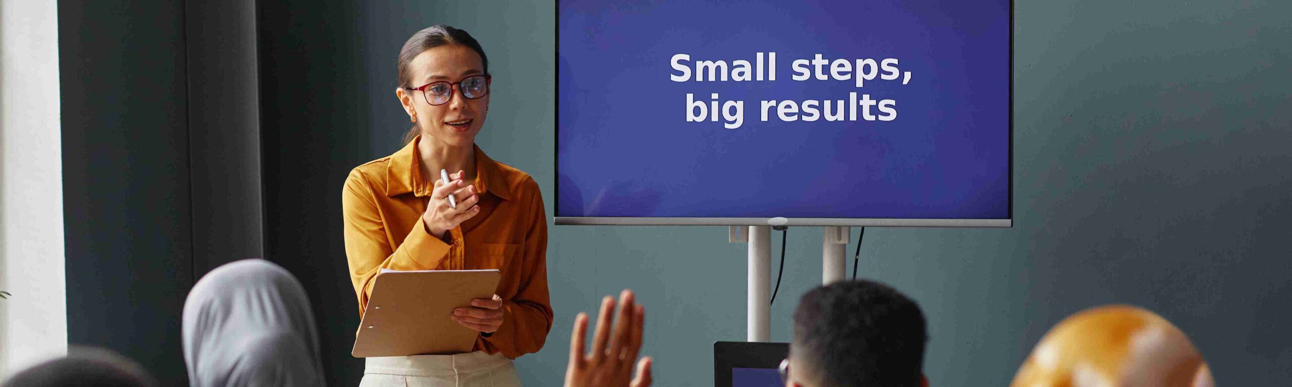 A woman presents in front of a screen displaying "Small Steps, Big Results," discussing the Scale-up Worker visa for UK jobs.