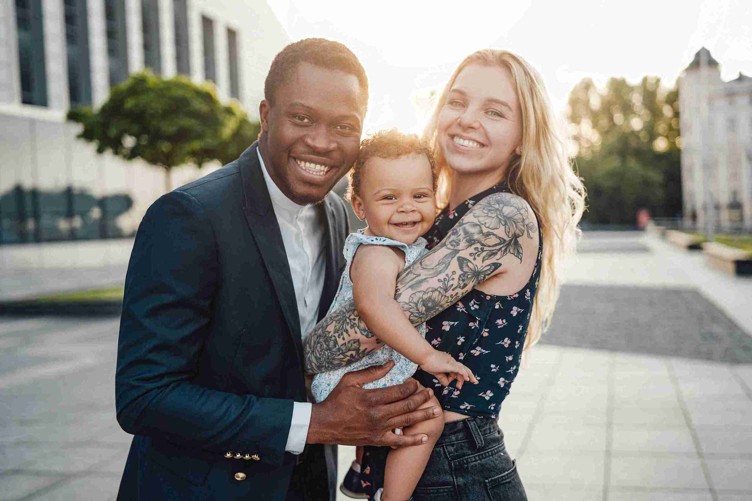A man and woman smile while holding a baby, posing together for a joyful family photo.