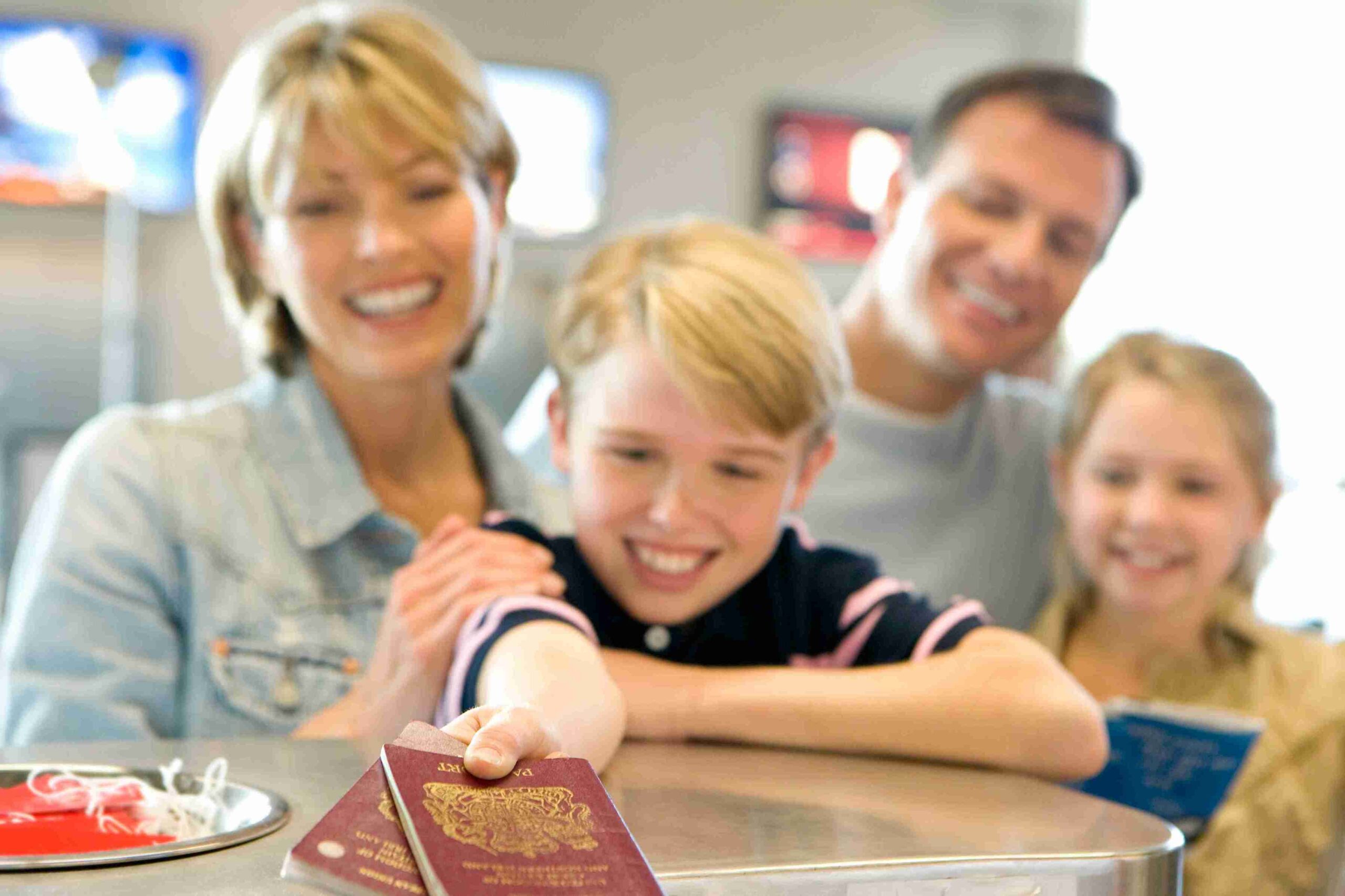 A family of four stands together at the airport, with UK Immigration signs visible in the background.