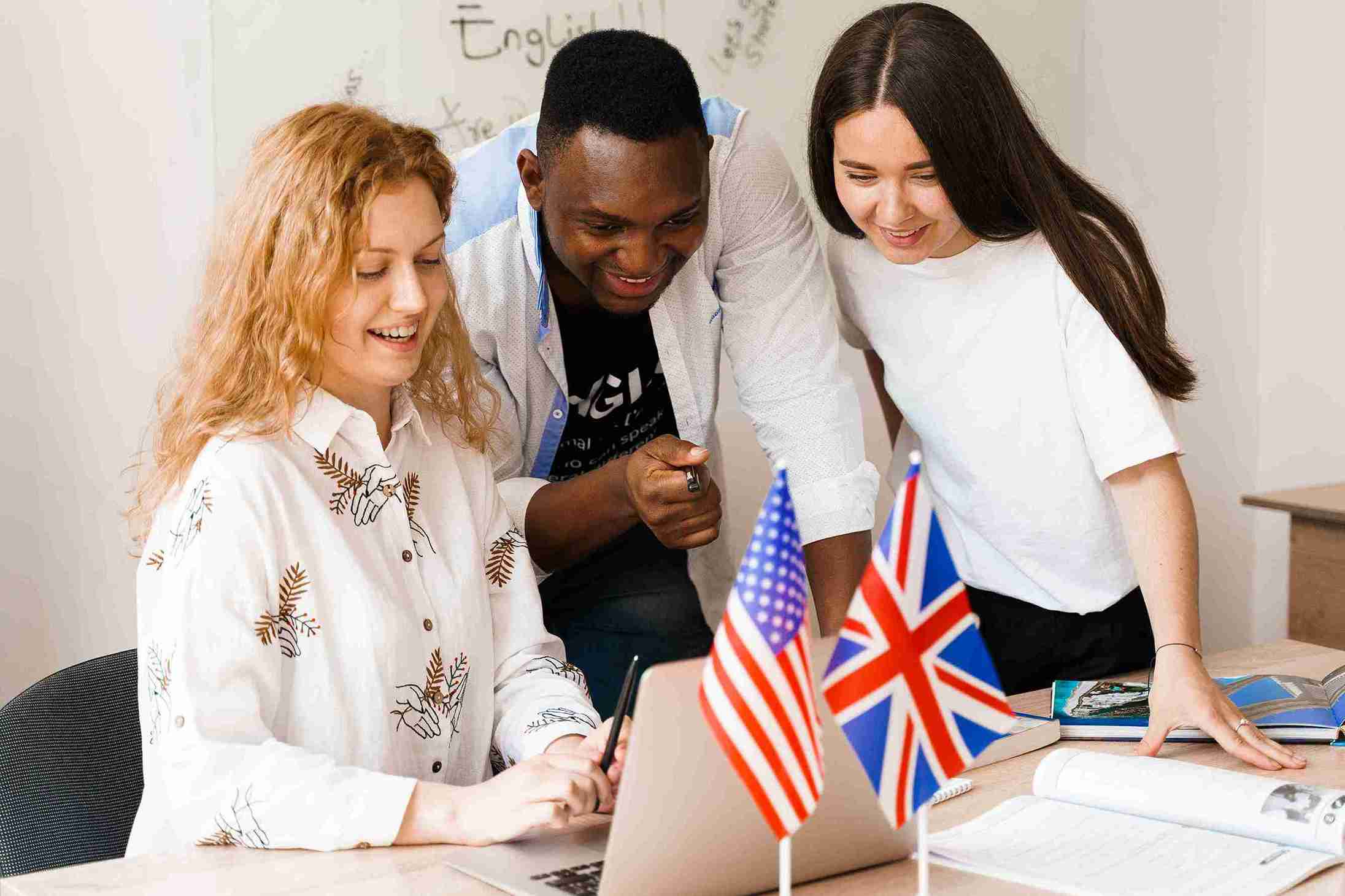 Three people, including a teacher, gather around a laptop displaying flags, discussing student study information.