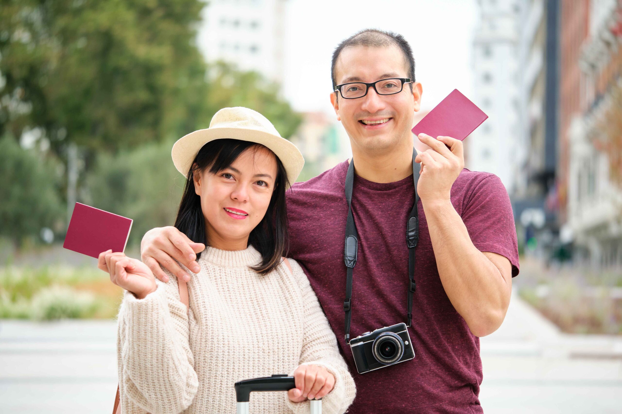 A man and woman smiling while holding up their passports, ready for travel.
