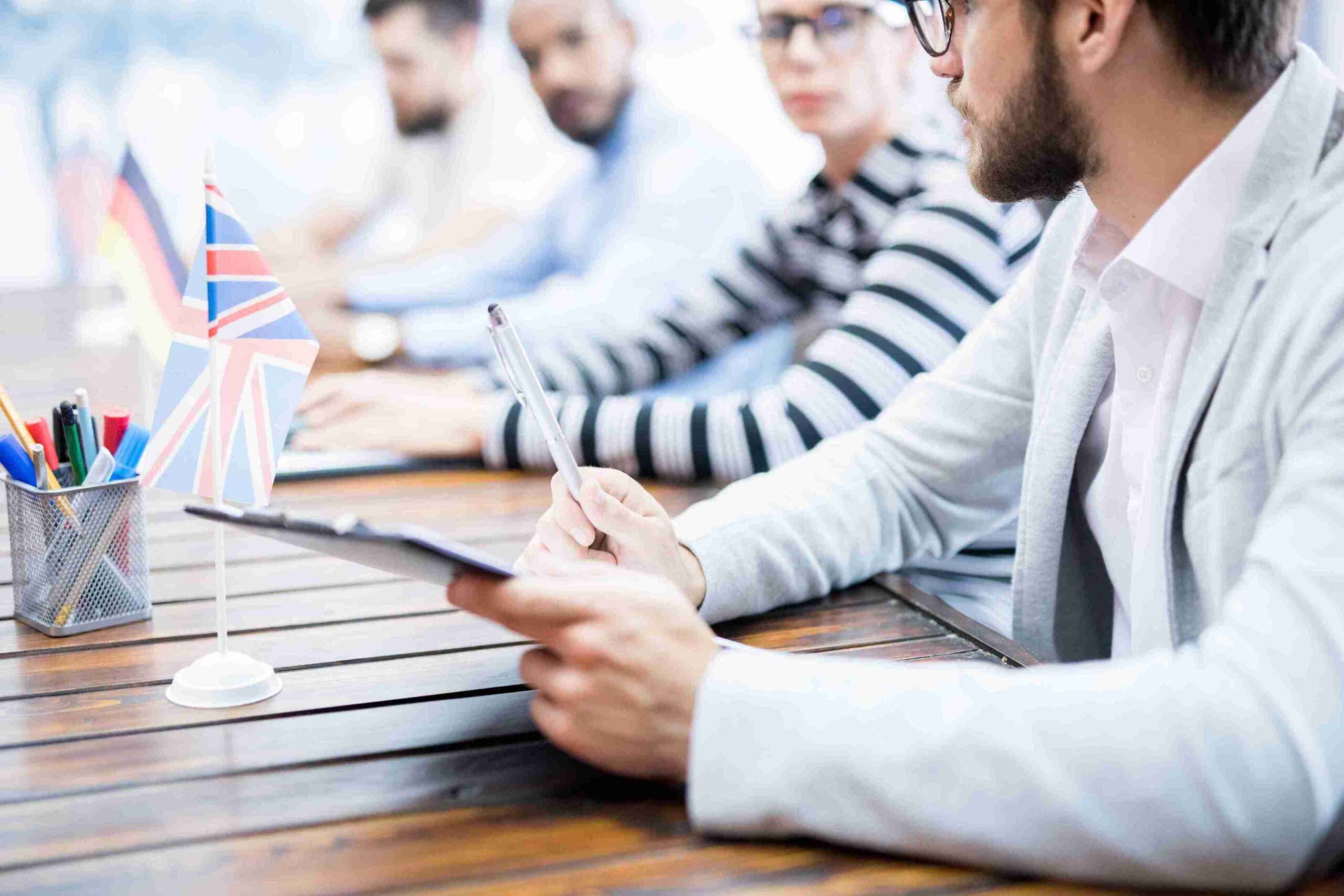 A group of people collaborates at a table, surrounded by pens and papers, discussing topics from "Studies, Work & Settlement