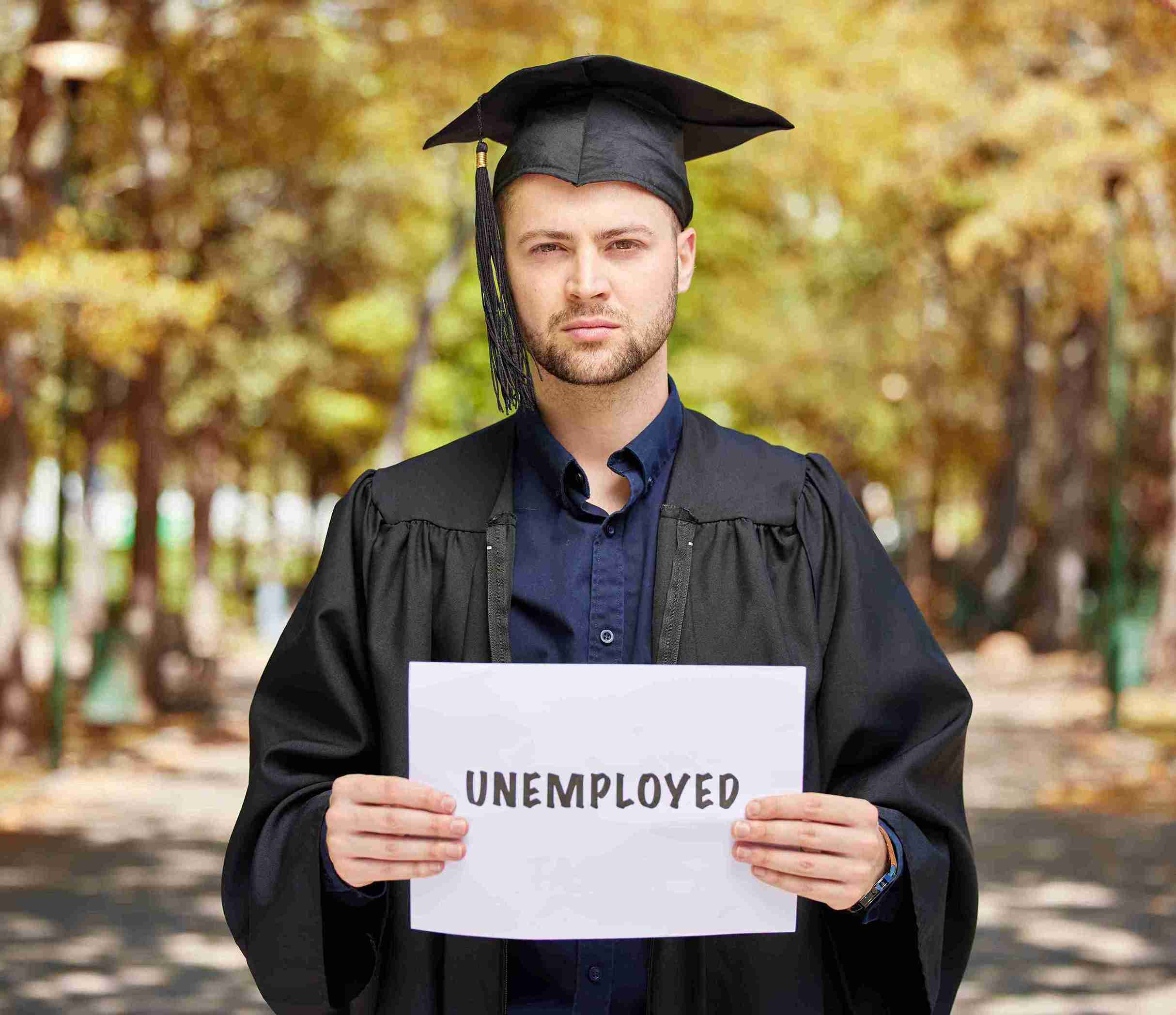 A man in a graduation gown holds a sign reading "unemployed," highlighting challenges faced by graduates in the UK