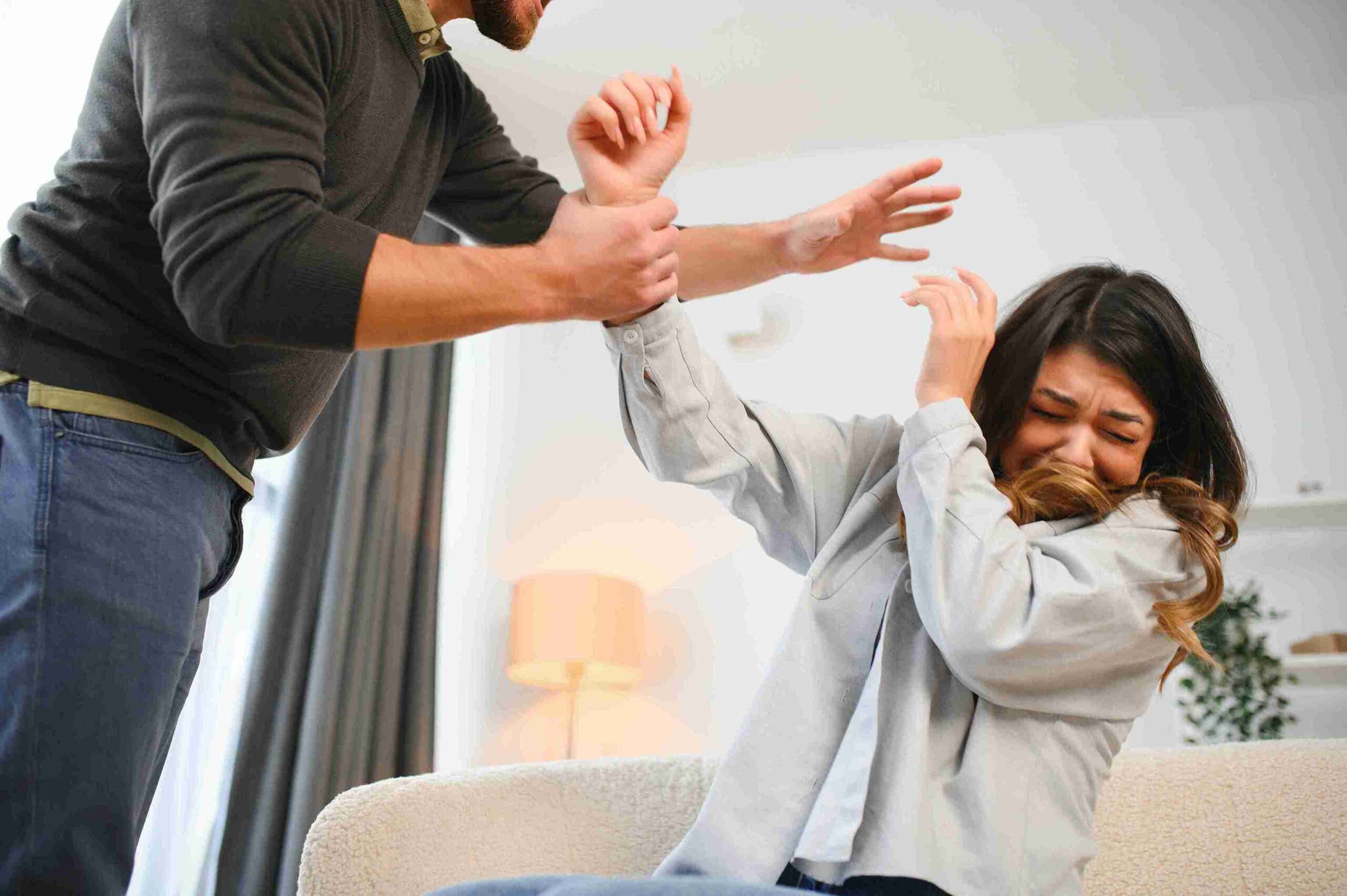 A man raises his fist at a frightened woman in a living room, depicting a scene of violence.