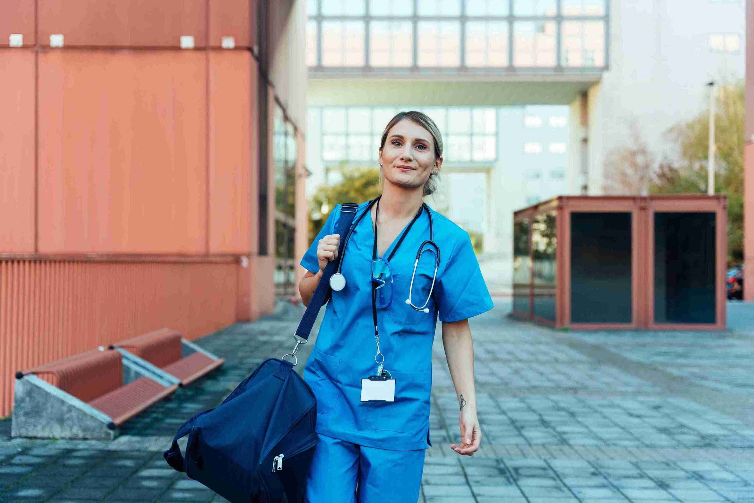 A female nurse in blue scrubs walking down a street, representing healthcare professionals in the community.