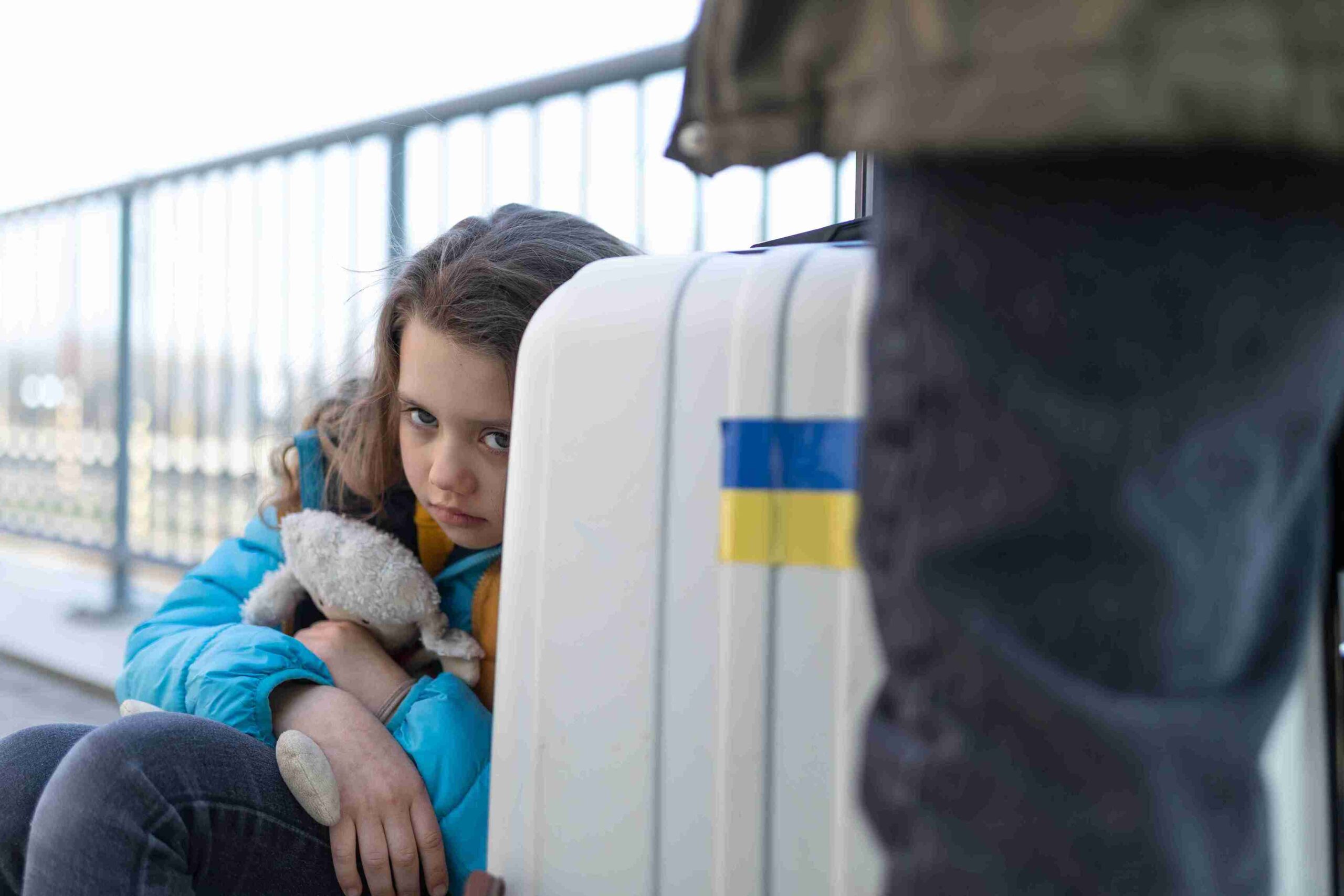 A young girl sits on the ground with a suitcase, conveying a sense of loss and uncertainty related to deportation.