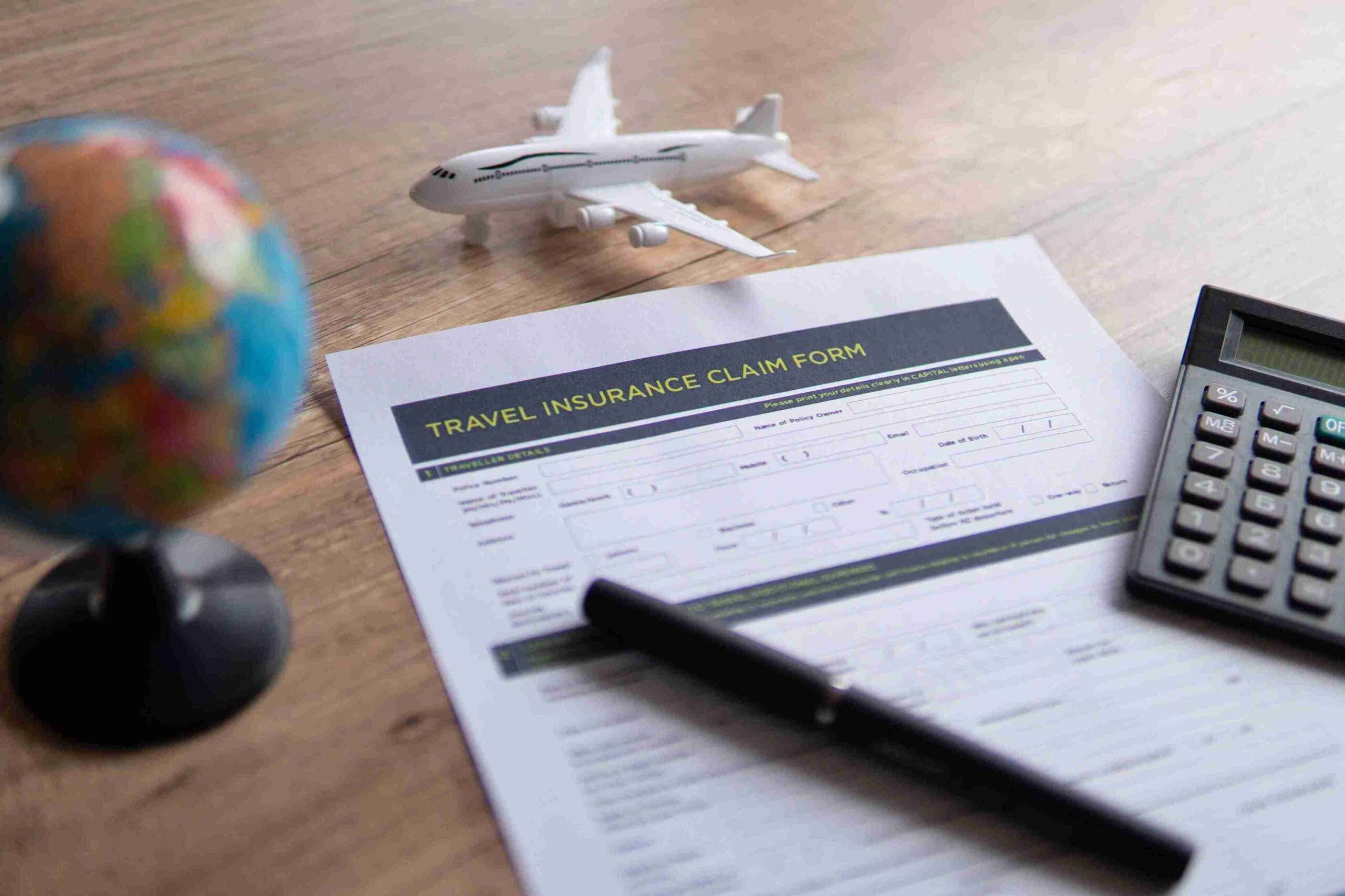 A travel insurance claim form on a wooden desk with a pen, miniature airplane, globe, and calculator, conveying a theme of travel planning and safety