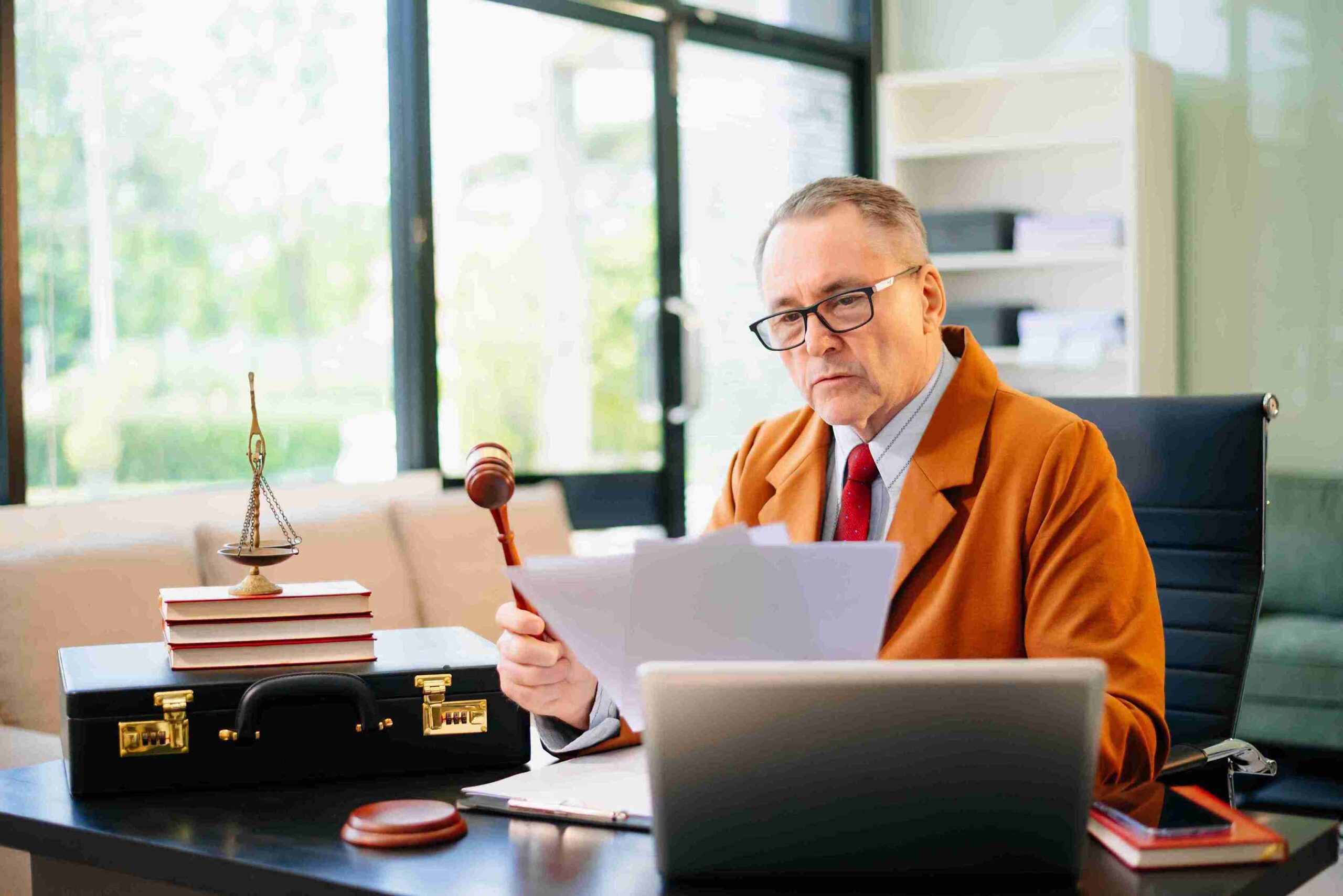 Older man in suit holding papers and gavel in legal office, representing legally secure authority arrangements protecting future personal decisions.