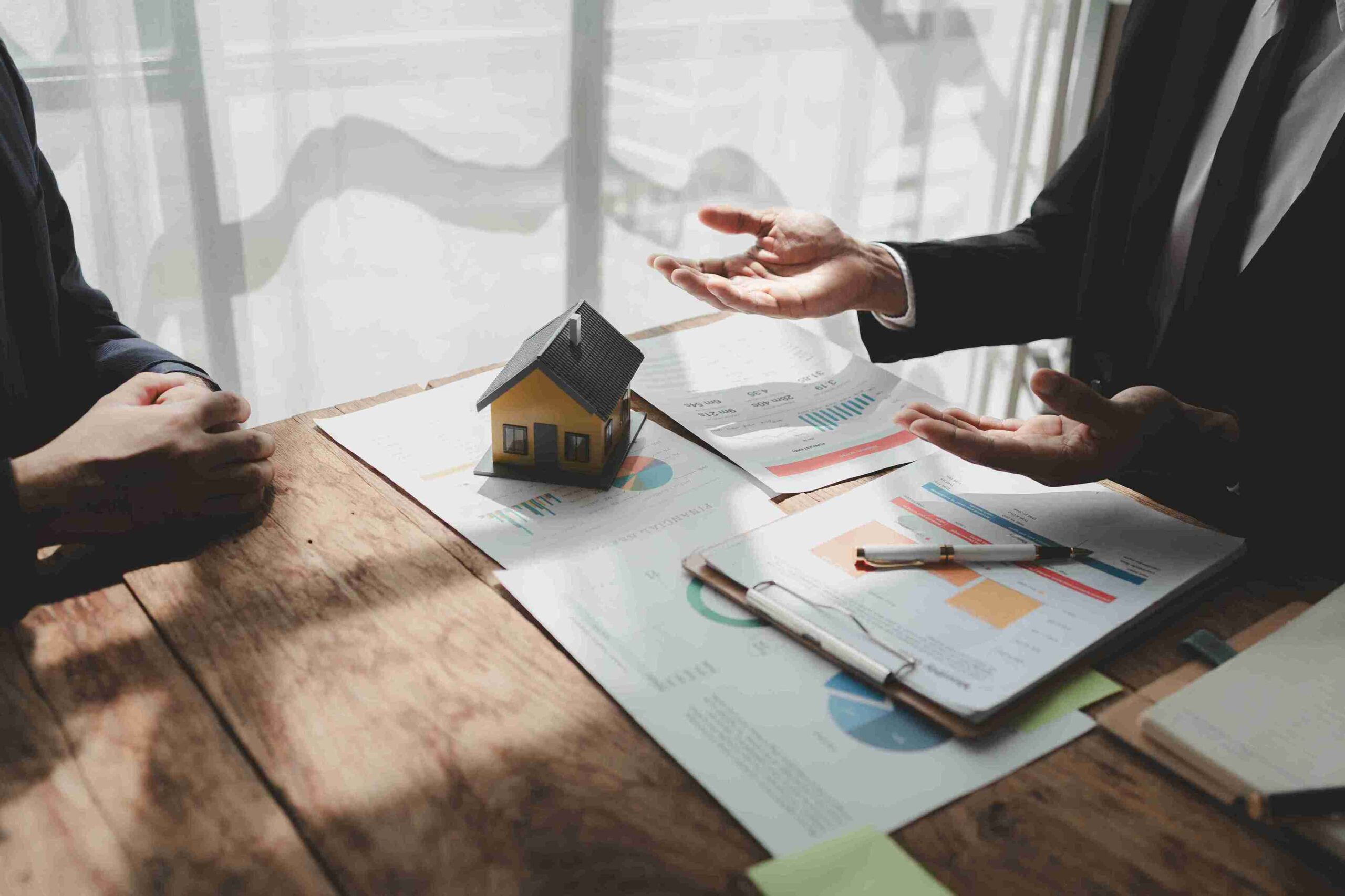 Two business people discussing property disputes while examining a house model at a table.