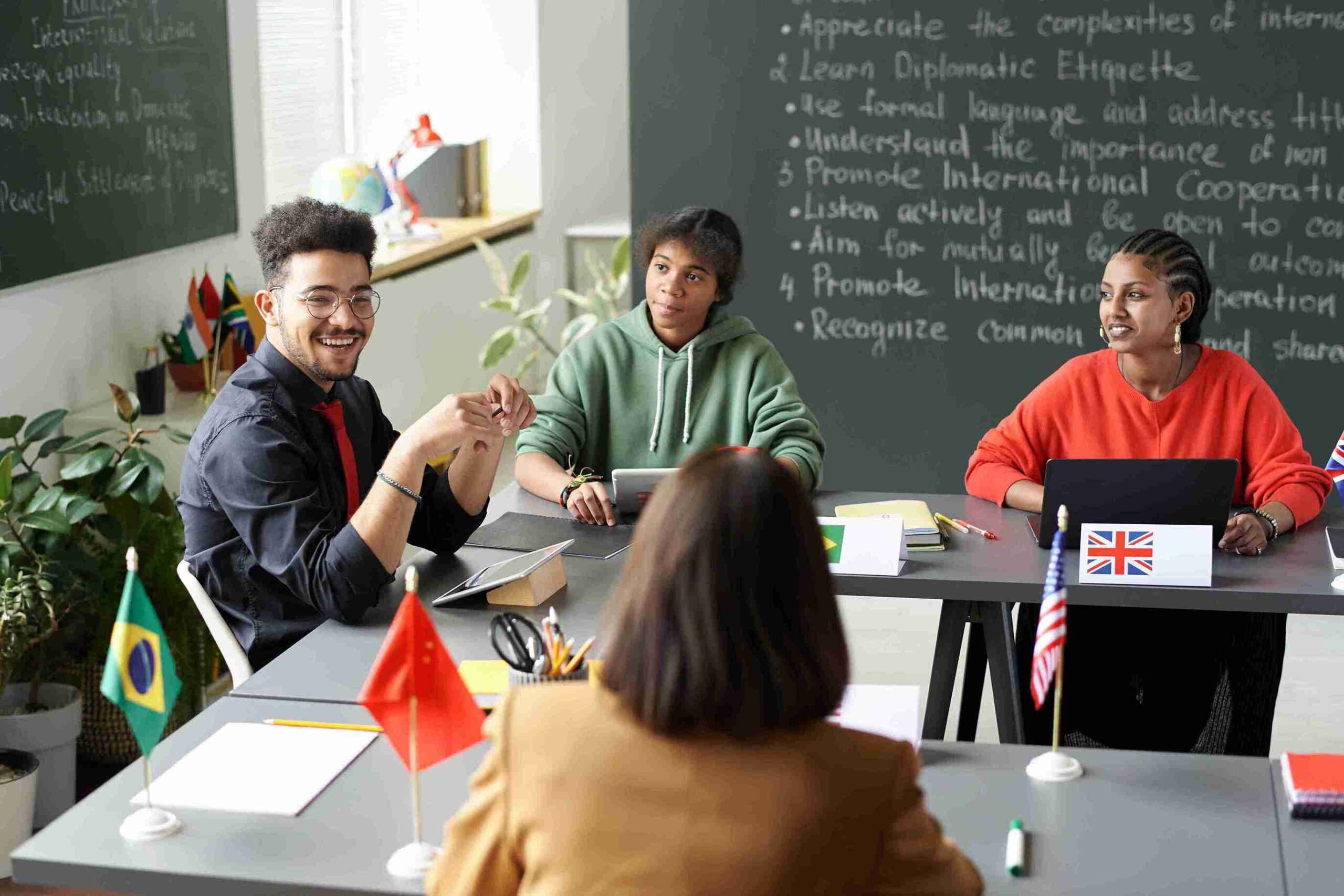 A group of people gathered around a table, engaged in discussion, with a chalkboard in the background.