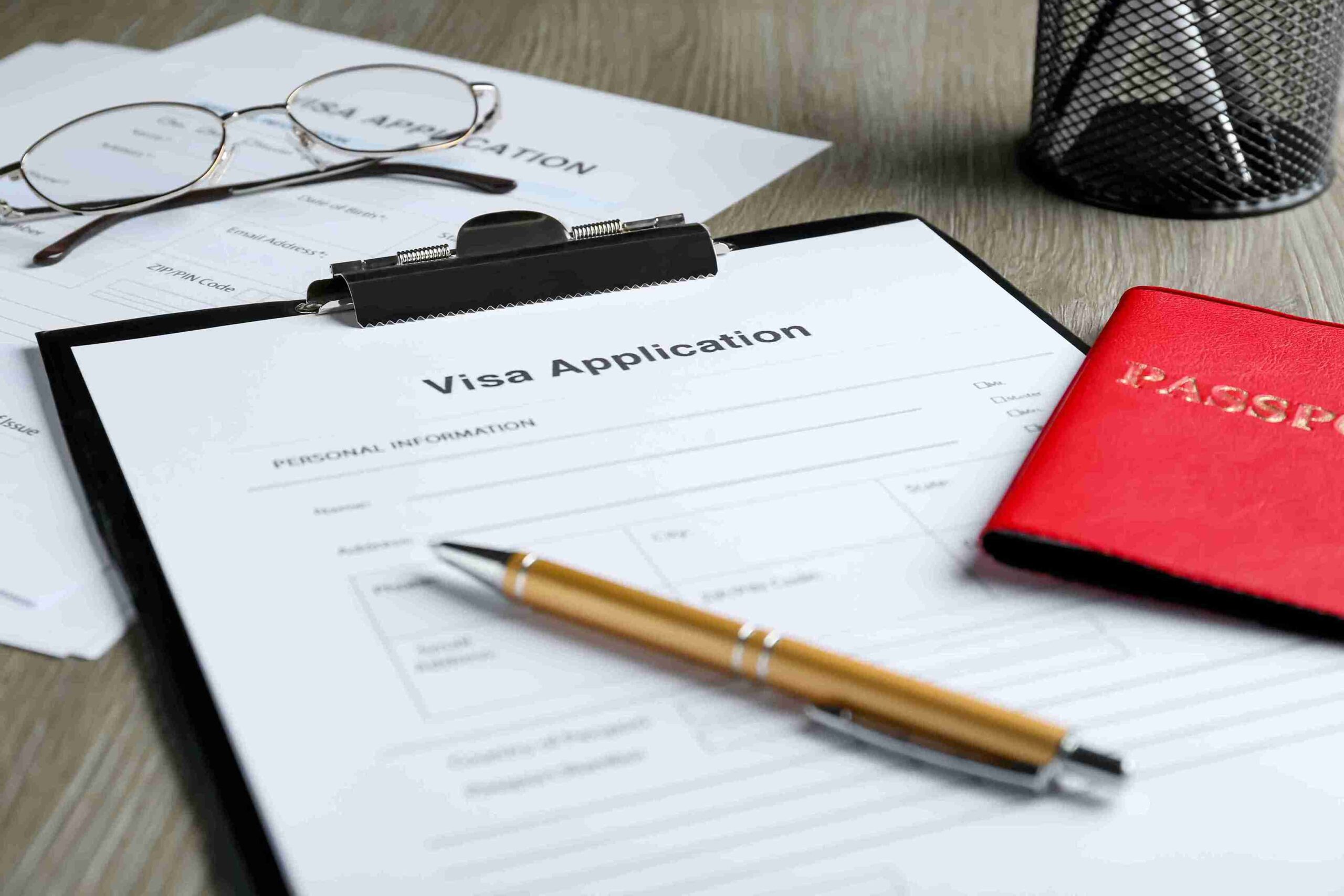 Visa application on clipboard with pen, red passport, and glasses, representing Innovator Founder Visa UK.