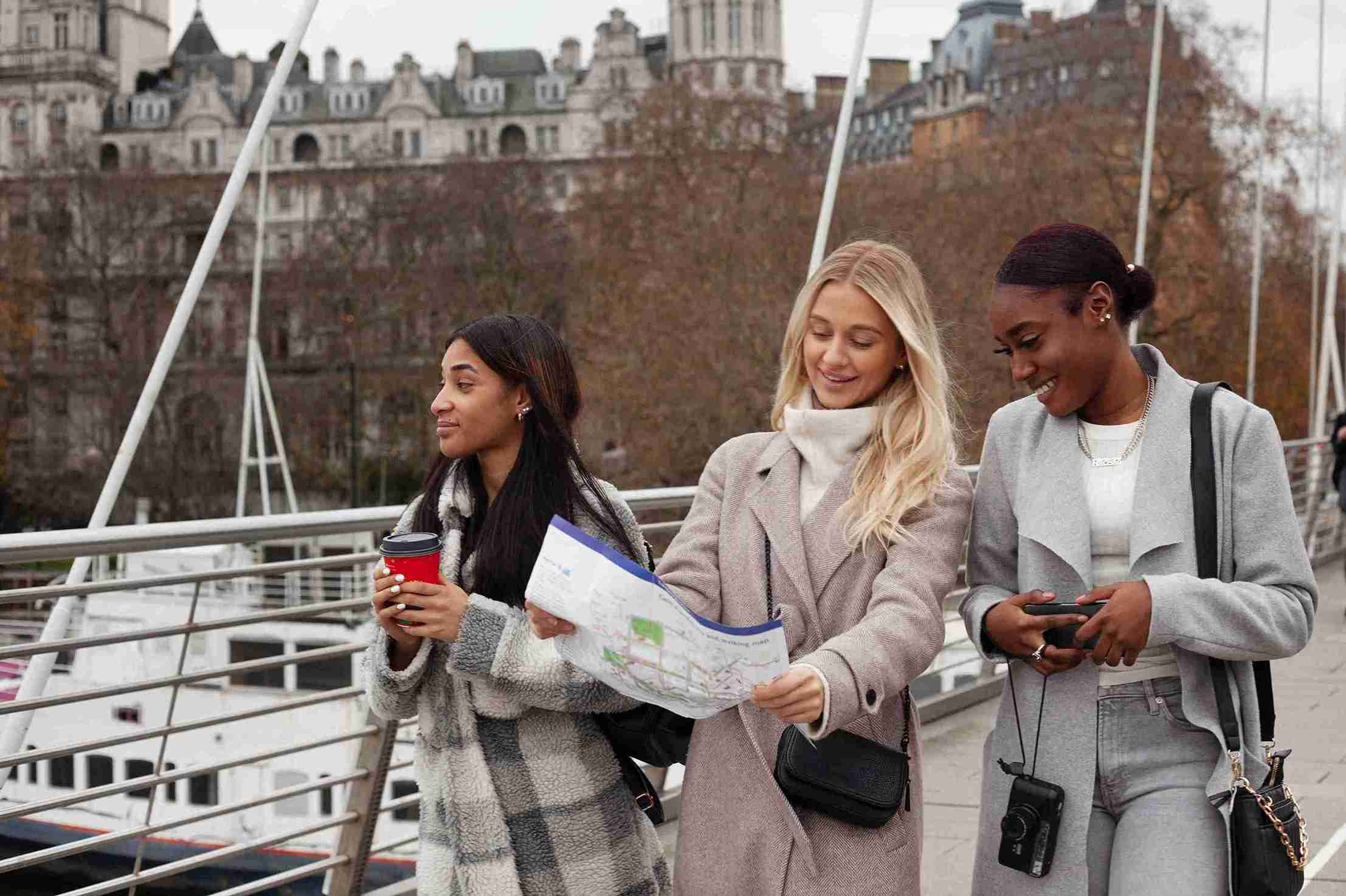 Three women on a bridge study a map, planning their visit to the UK for a tourist visa.