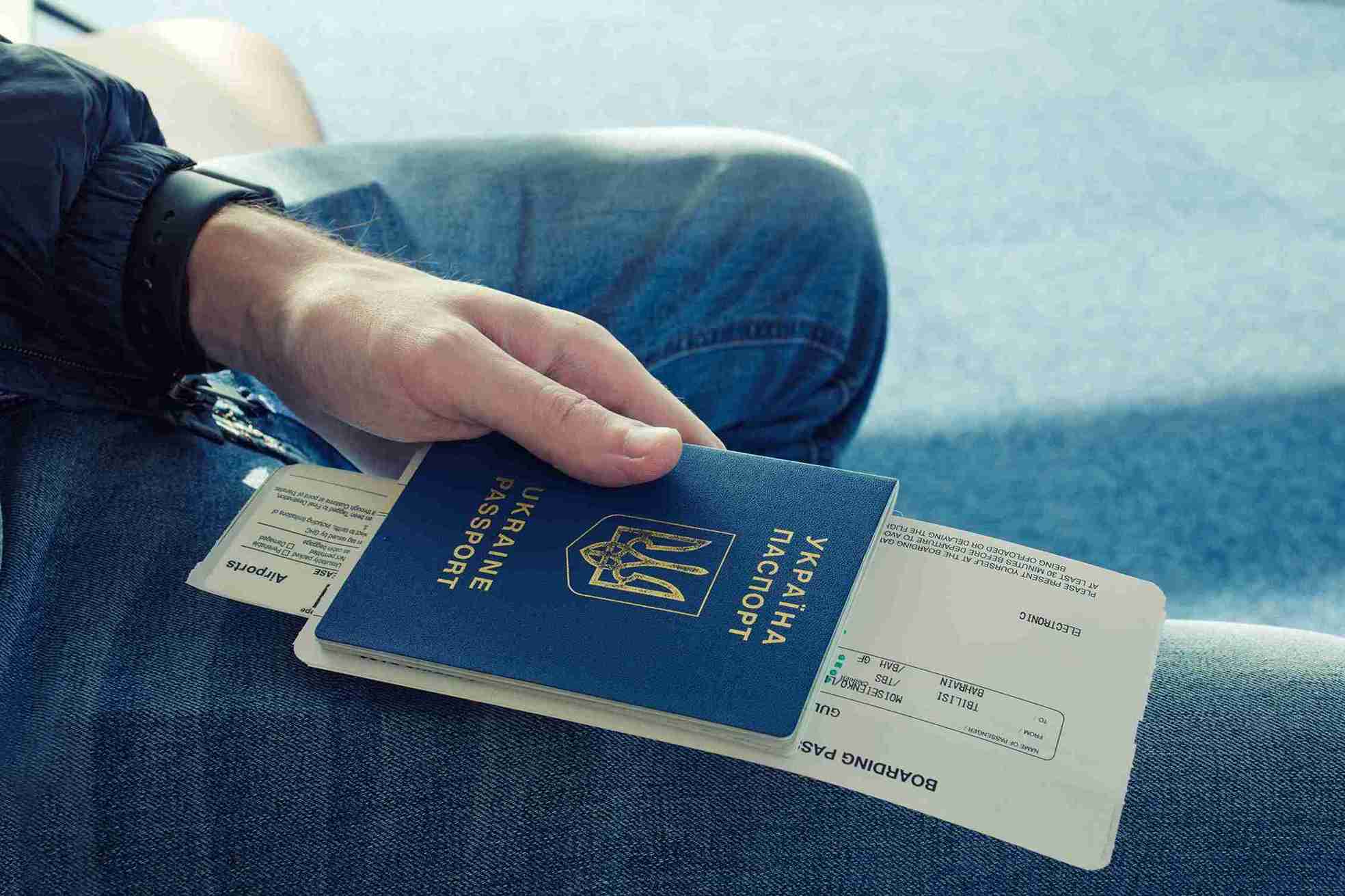 A person holding a passport, ready for travel, with a focused expression and a blurred background of an airport.