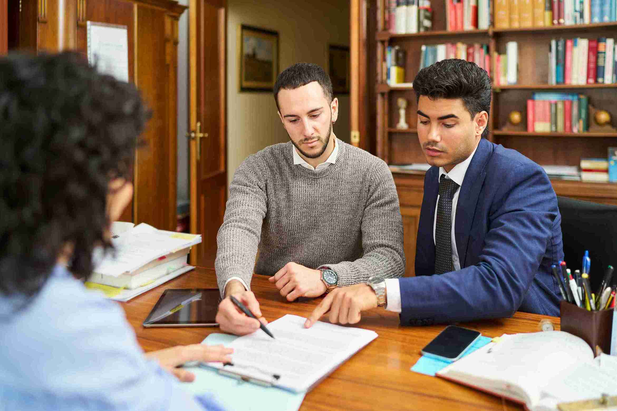 Three people reviewing documents at a table with books and pens, representing solicitors guiding clients through the process with an action plan.