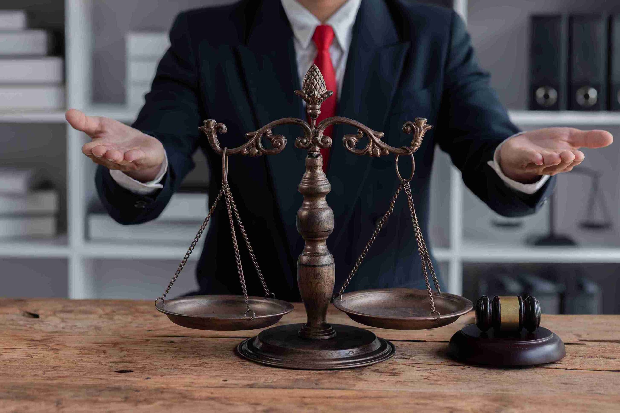 Person in suit and red tie standing behind balanced scale with gavel, representing tribunal representation.