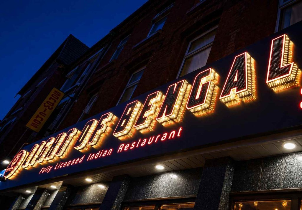 Neon sign reading "the palace of england" glowing brightly against a dark background.