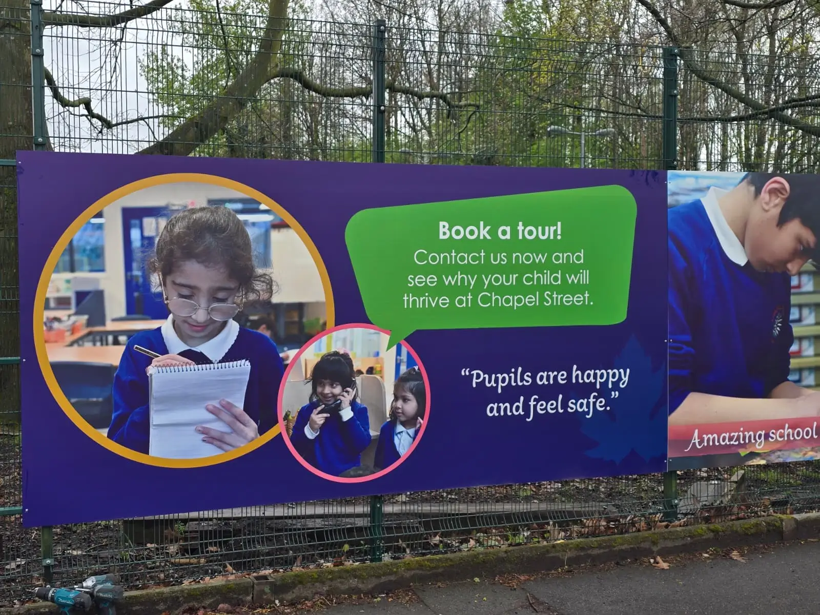 A large banner promoting a school, displayed prominently in a park setting, attracting visitors and families.