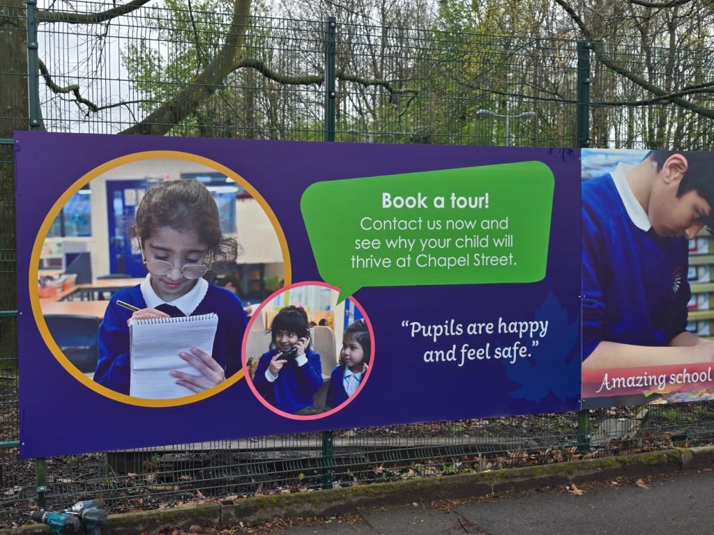 A large banner promoting a school, displayed prominently in a park setting, attracting visitors and families.