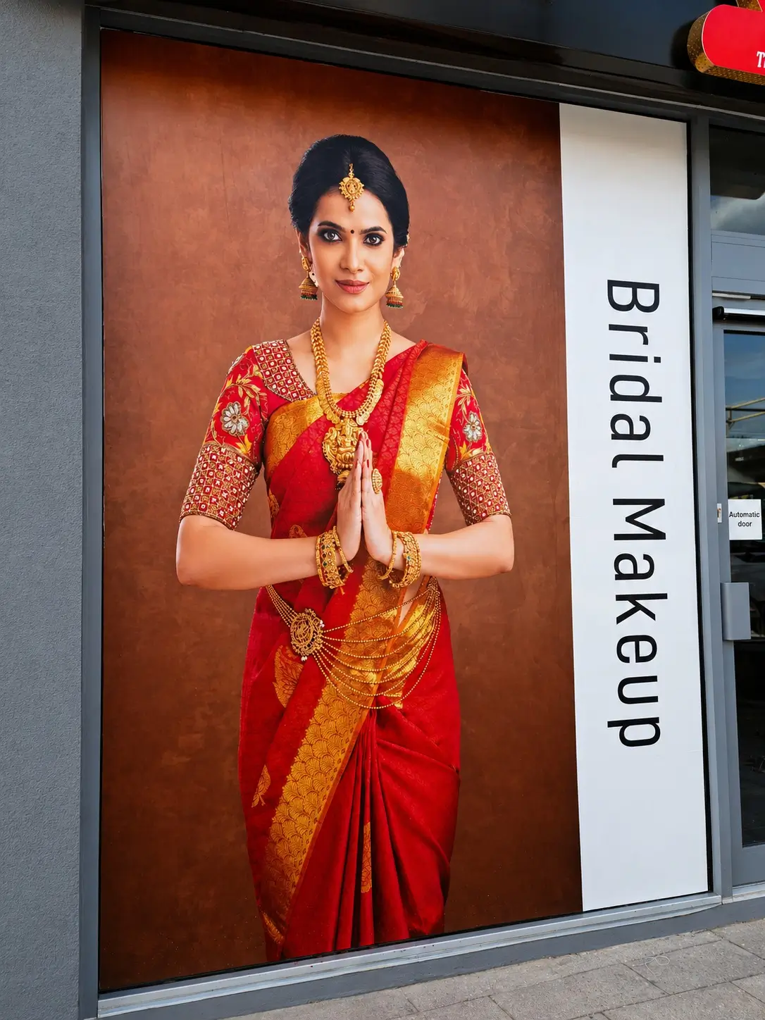 A woman in a colorful sari stands in front of a store window, gazing at the displayed items with interest.